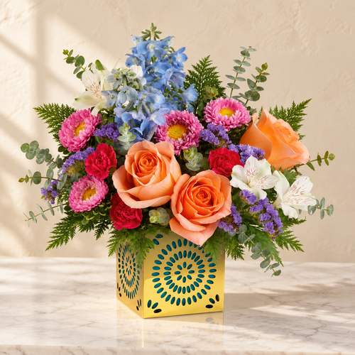 Peach roses, blue delphinium, white alstroemeria and pink carnations in a gold cut-out cube