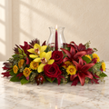 Yellow cymbidium orchids, red roses and burgundy lilies around a candle in a glass hurricane