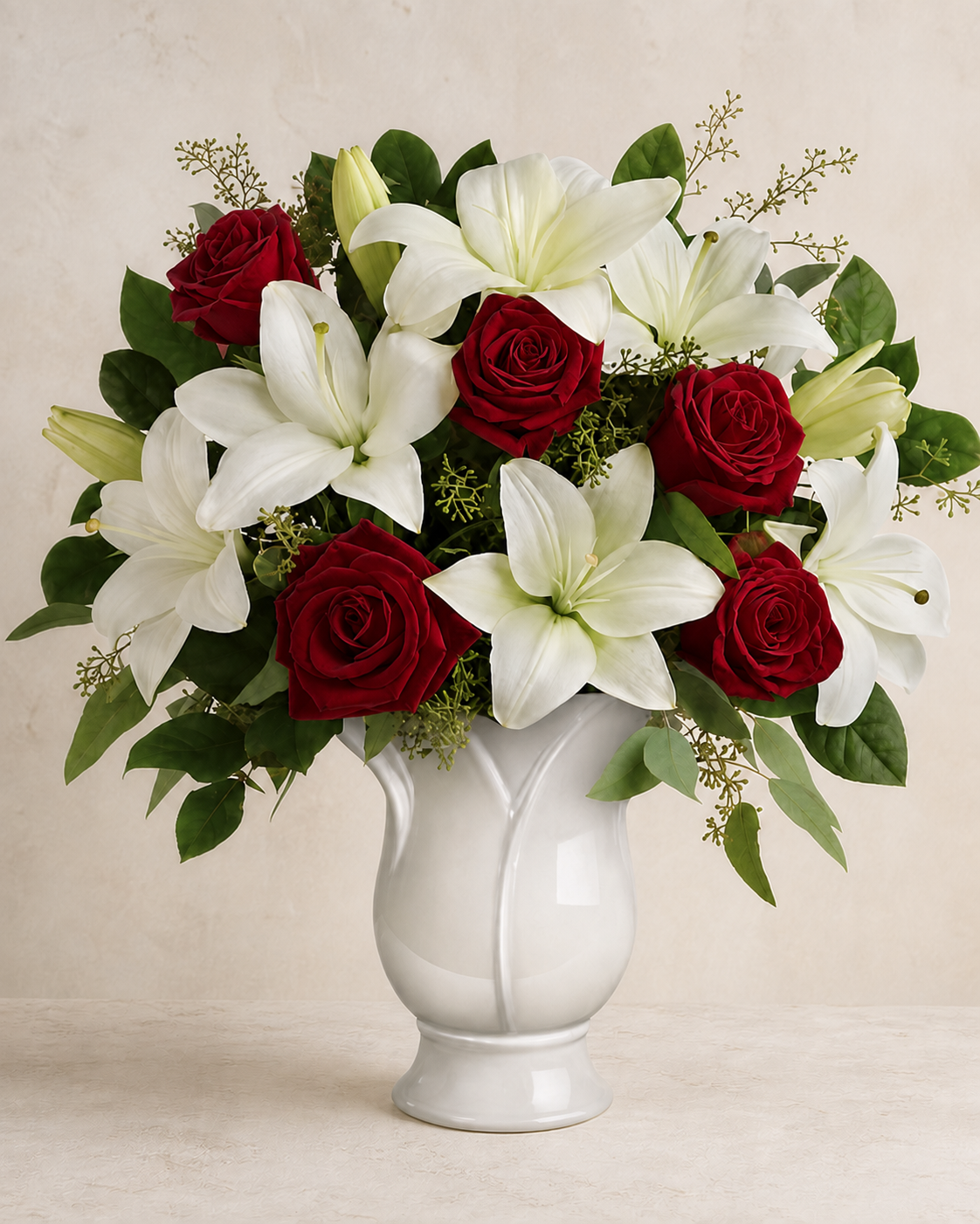 Velvet-red roses and cream-white lilies in a white ceramic pedestal vase