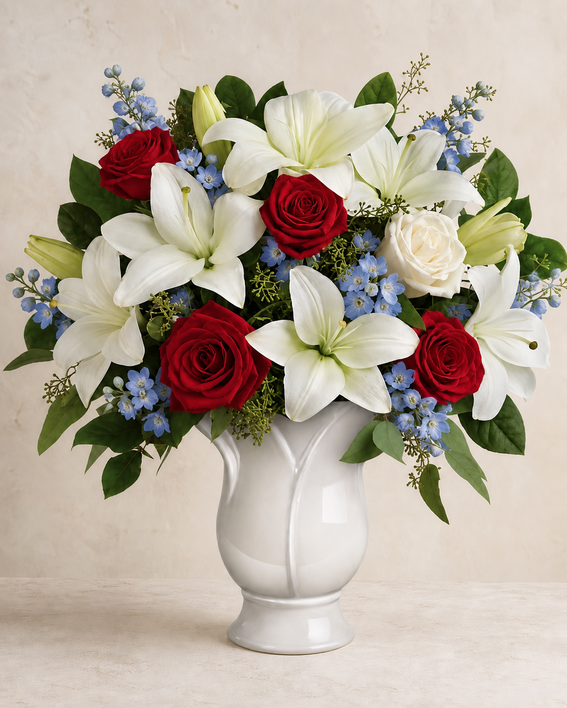 Natural red roses, cream-white lilies and roses, and powder-blue delphinium in a white ceramic pedestal vase