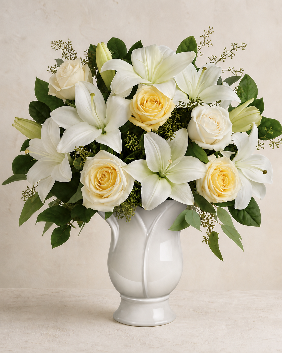Butter-yellow roses and cream-white lilies in a white ceramic pedestal vase