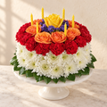 Flower birthday cake of white mums, red carnations, orange spray roses and a yellow rose with yellow candles on a white cake stand