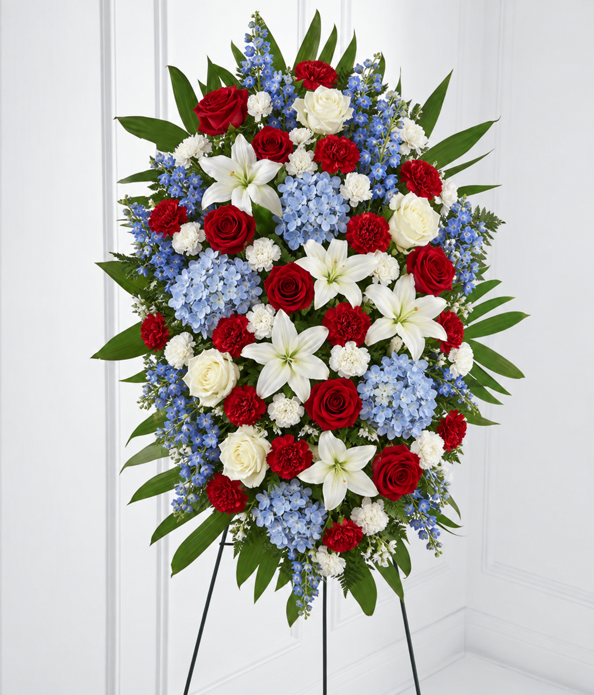 Natural red roses and carnations, cream-white lilies and roses, and powder-blue flowers in a standing spray